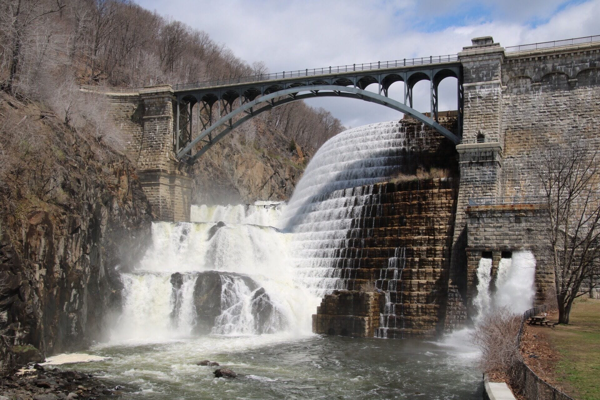 A dam with a waterfall, a stone bridge, and a river.