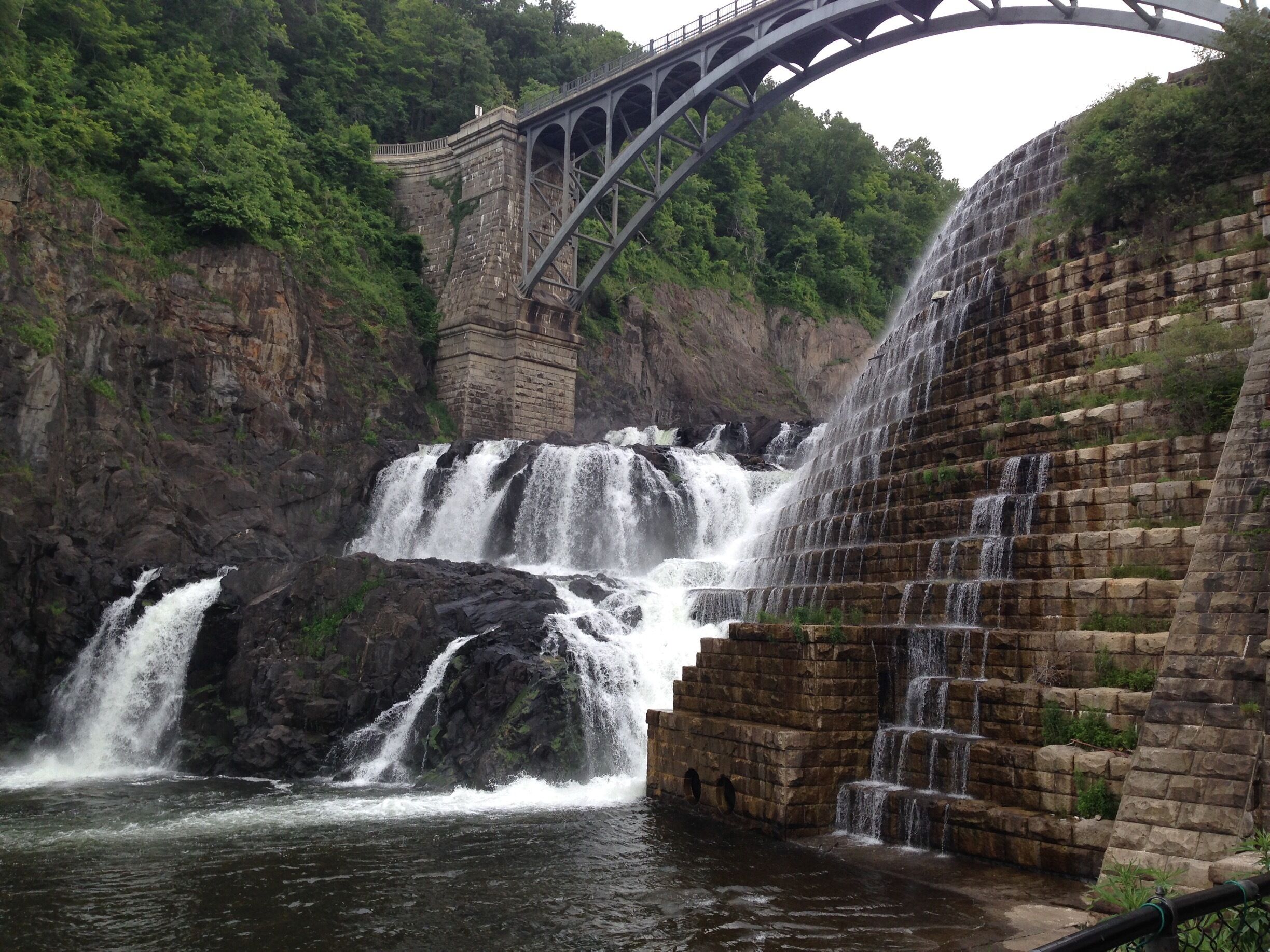 A multi-tiered waterfall with a stone retaining wall and a bridge.