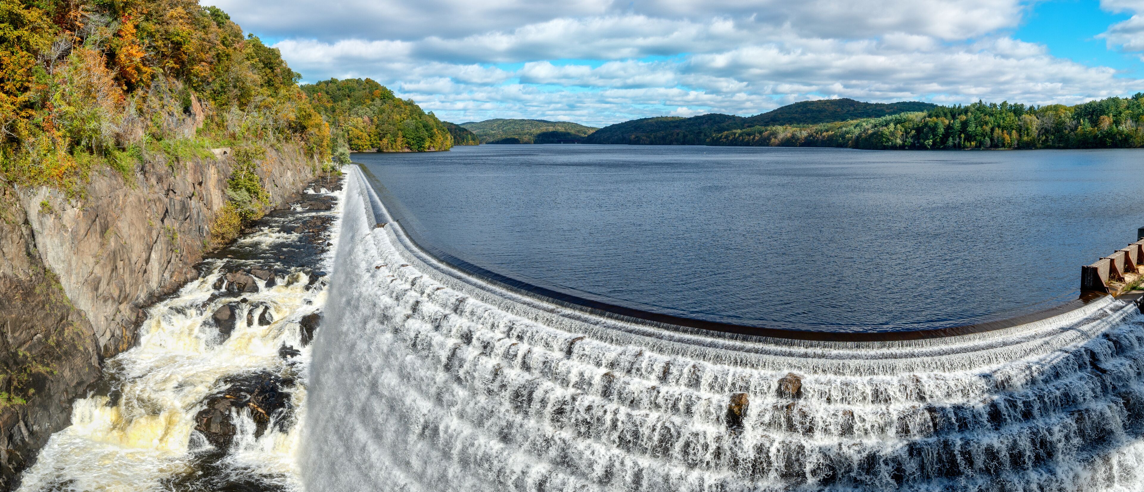 A dam with a waterfall, a river, and surrounding hills.