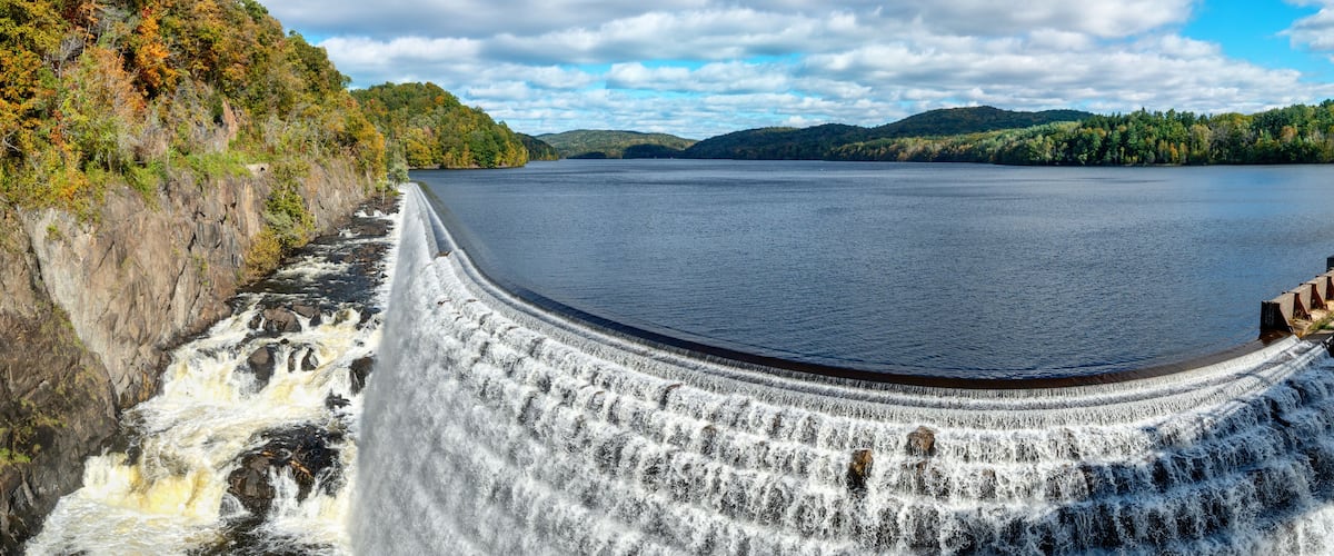 A dam with a waterfall, a river, and surrounding hills.