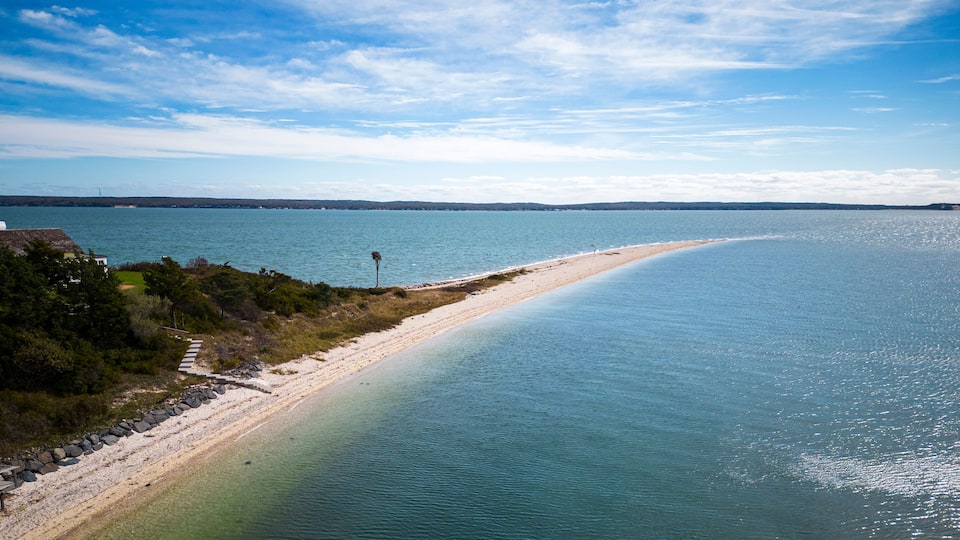 A coastal landscape with a sandy beach, clear blue water, and a distant lighthouse.