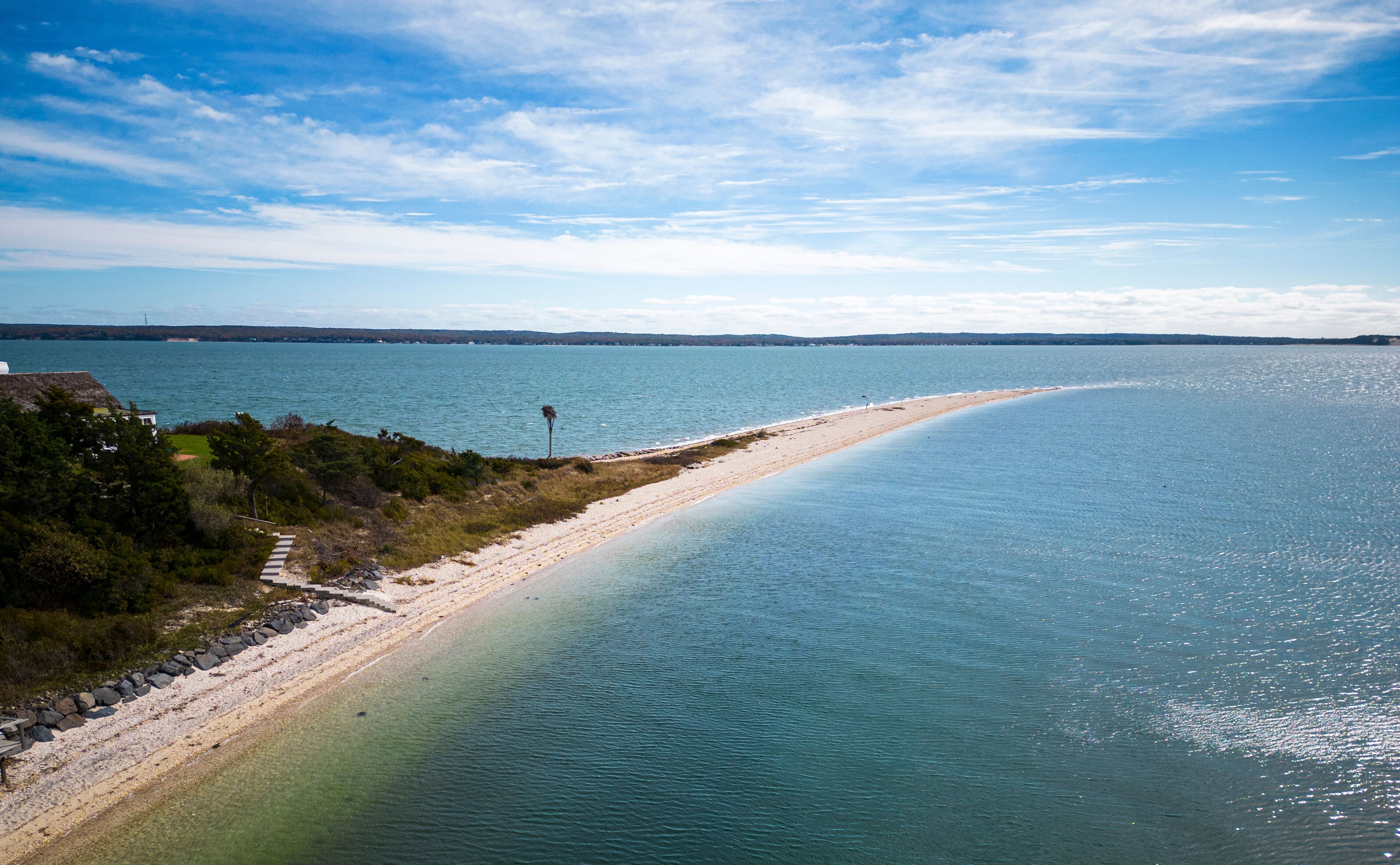 A coastal landscape with a sandy beach, clear blue water, and a distant lighthouse.