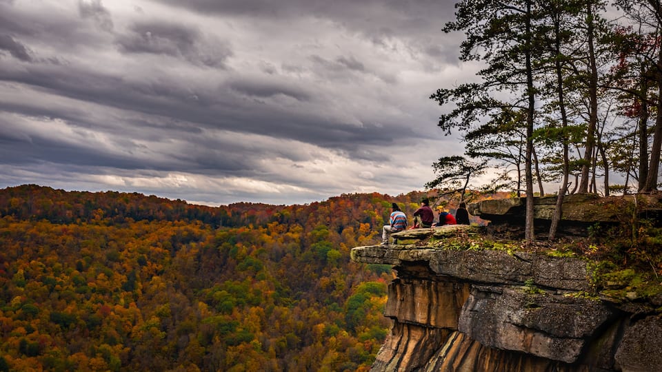 A rocky cliff overlooking a forested valley with autumn foliage.