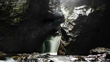 A waterfall cascading through a rocky gorge with sunlight filtering through.