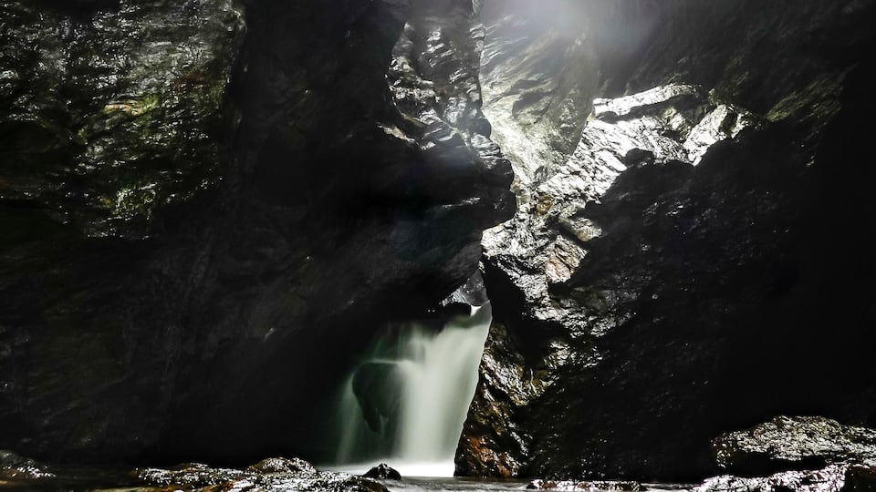 A waterfall cascading through a rocky gorge with sunlight filtering through.