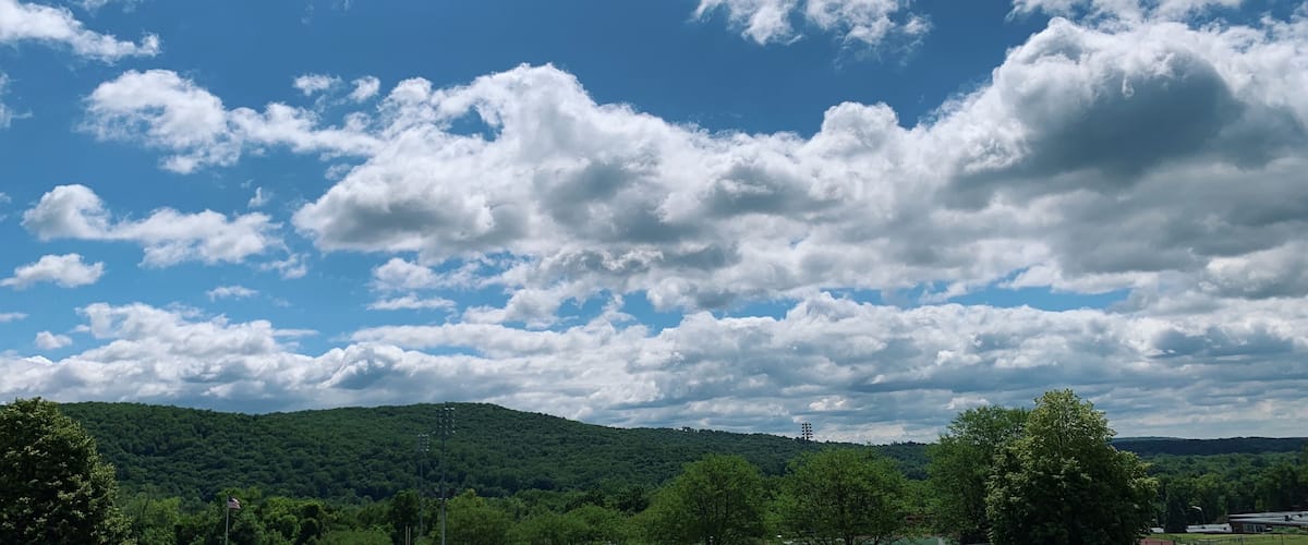 A landscape with a clear blue sky, scattered clouds, and a green hill in the distance.