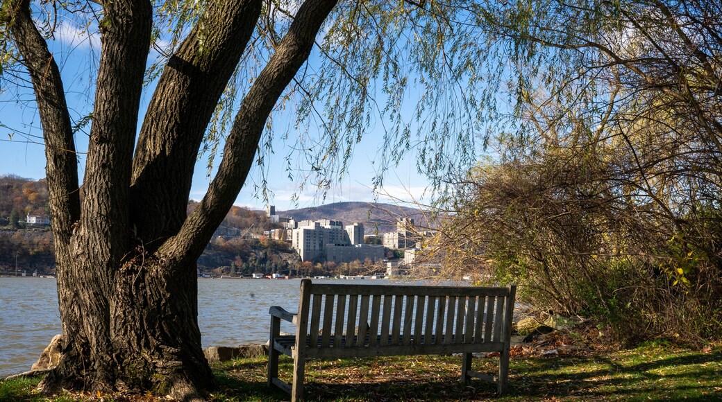 Garrison, NY - USA - Nov. 12, 2022 Landscape view of a wooden bench at Garrison Landing's riverside park, with West Point and the river in the distance.