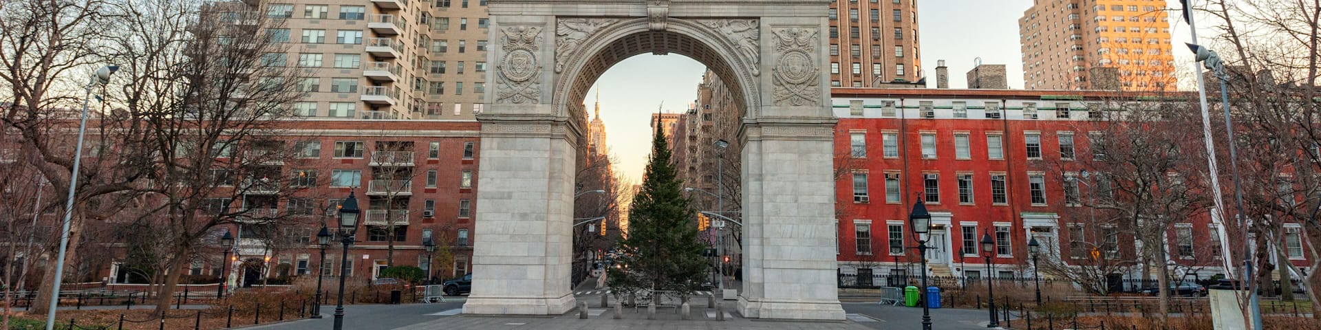 An archway with intricate carvings, surrounded by tall buildings and leafless trees.