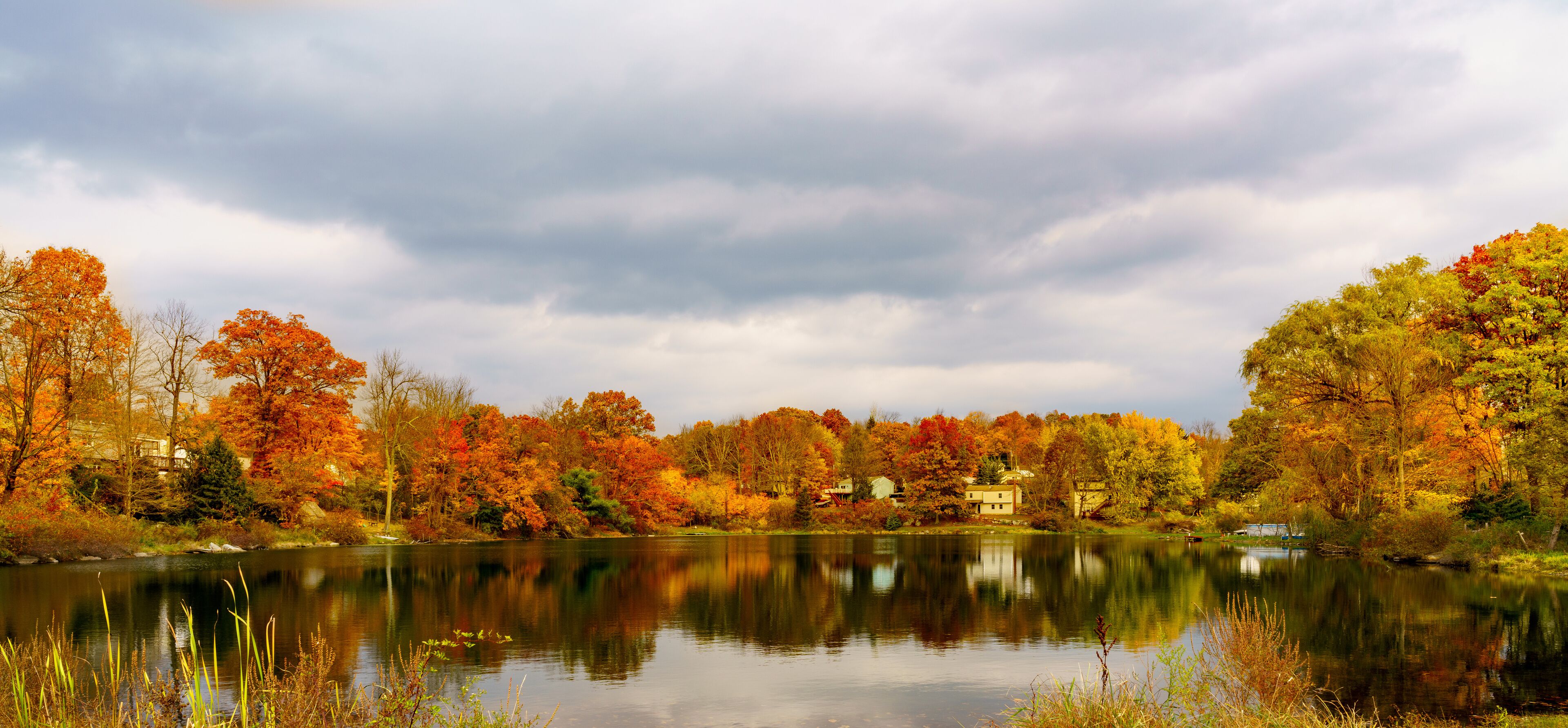 A calm lake surrounded by autumn-colored trees and houses in the background.