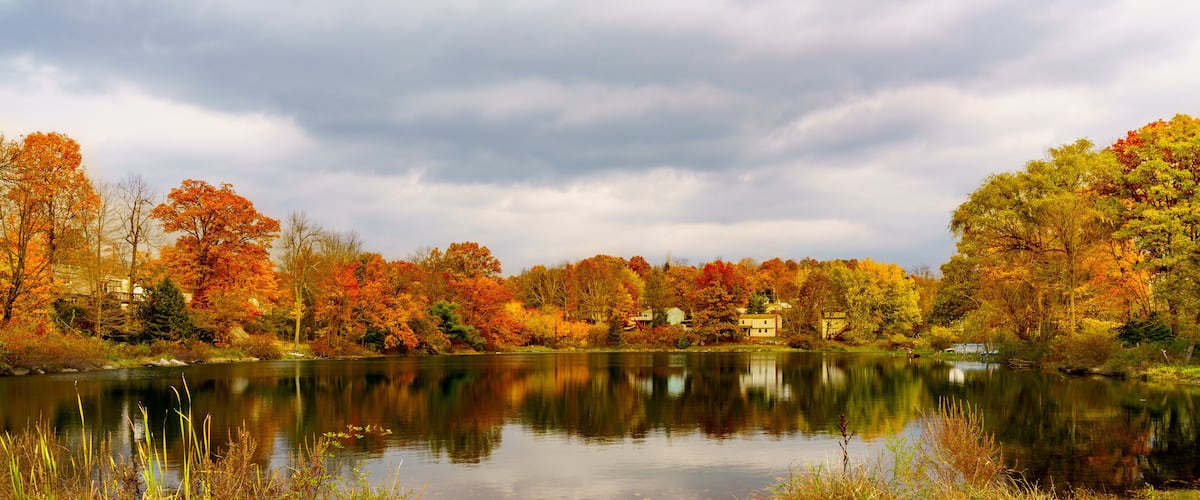 A calm lake surrounded by autumn-colored trees and houses in the background.