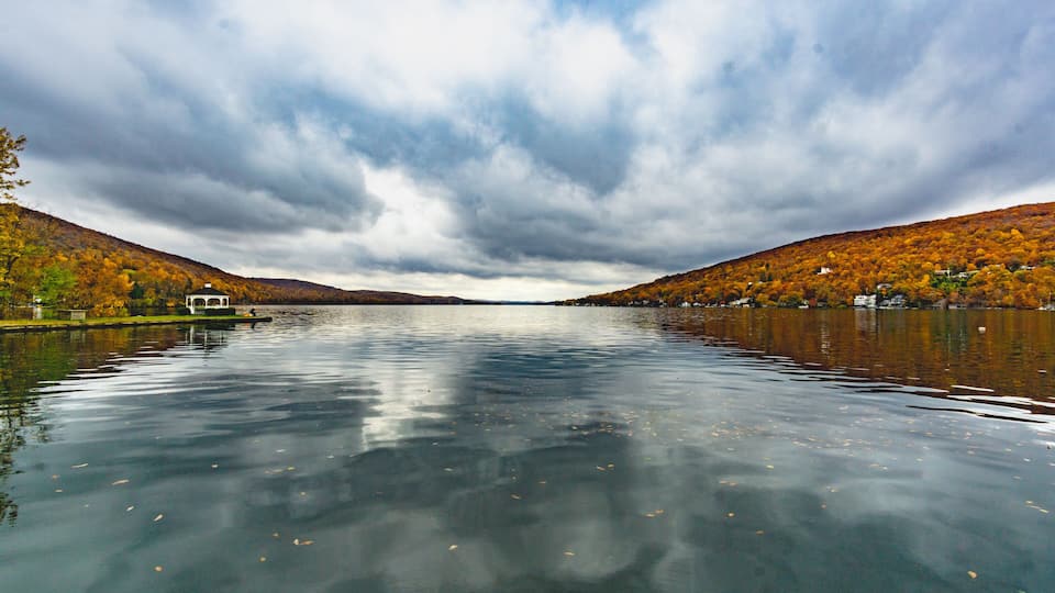A calm lake surrounded by autumn-colored hills and a gazebo on the left.
