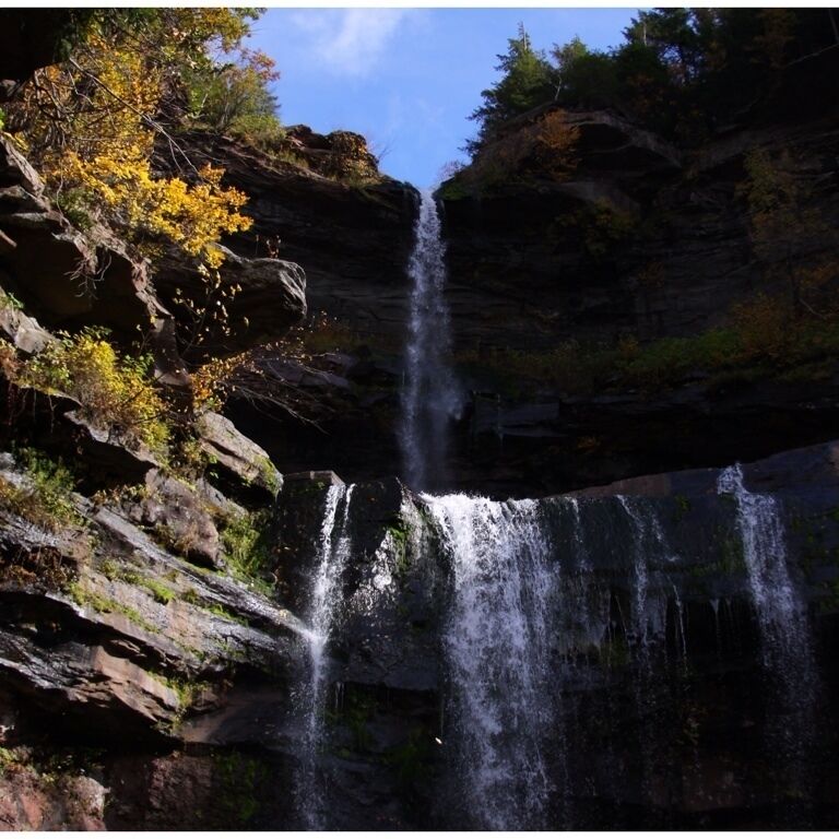 A waterfall cascading down a rocky cliff surrounded by autumn foliage.