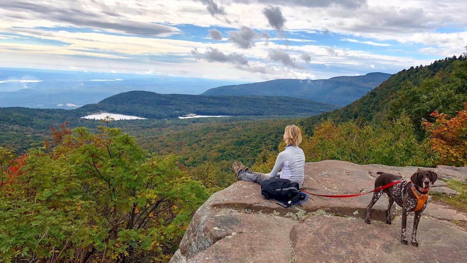 A person sitting on a rock overlooking a mountainous landscape with a lake and autumn foliage.
