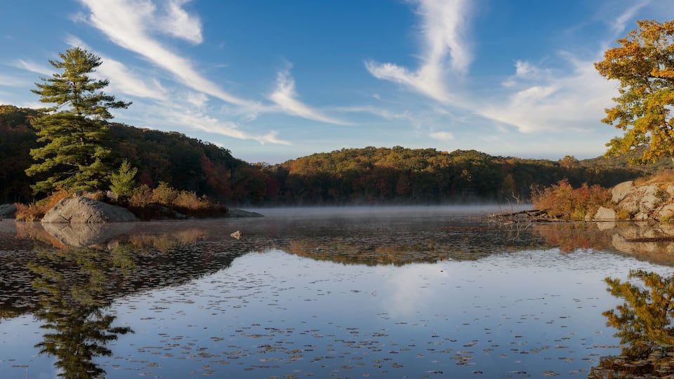 A calm lake surrounded by autumn foliage and a clear sky.