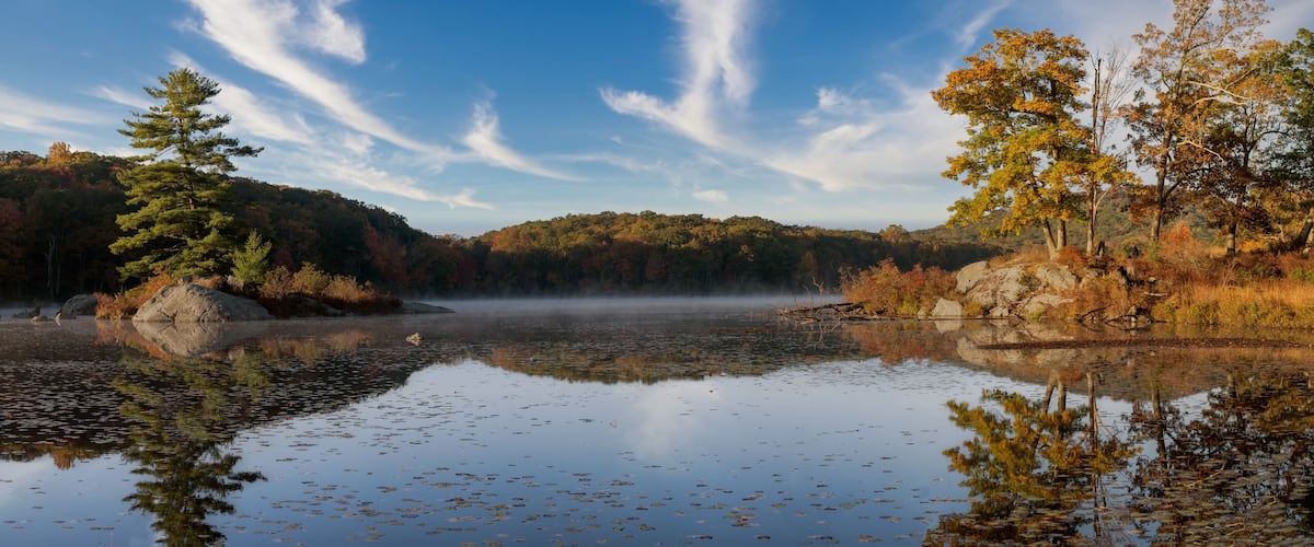 A calm lake surrounded by autumn foliage and a clear sky.