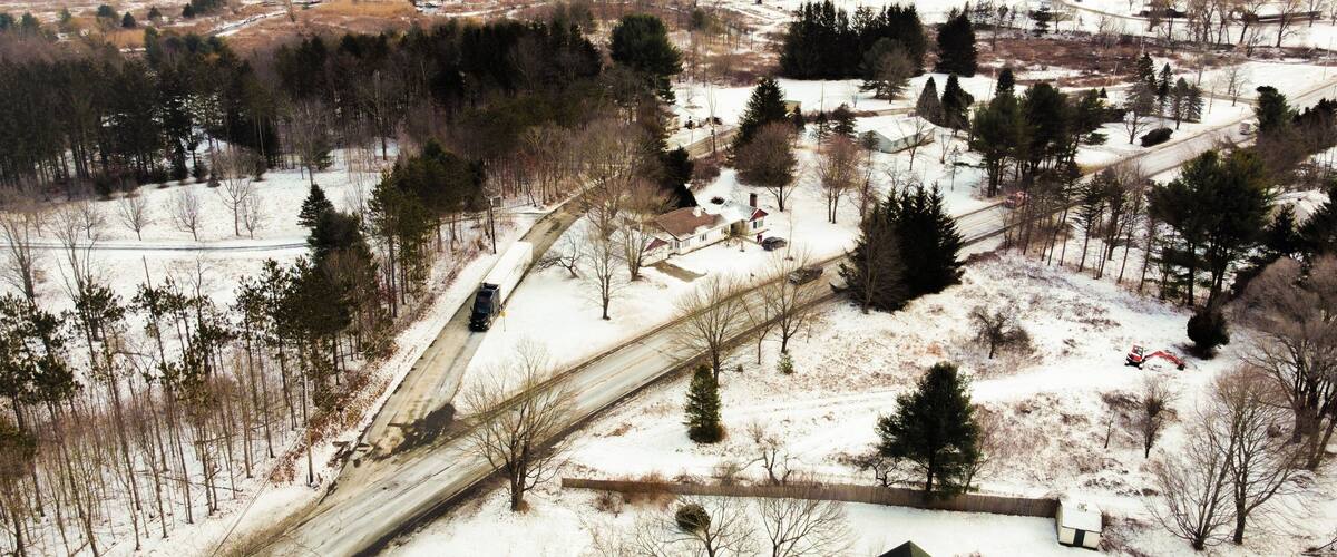 A rural landscape with snow-covered fields, a winding road, and scattered trees.