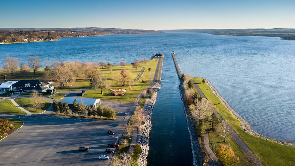 A river with a long pier, a parking lot, and buildings on the left bank.