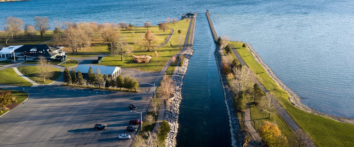 A river with a long pier, a parking lot, and buildings on the left bank.