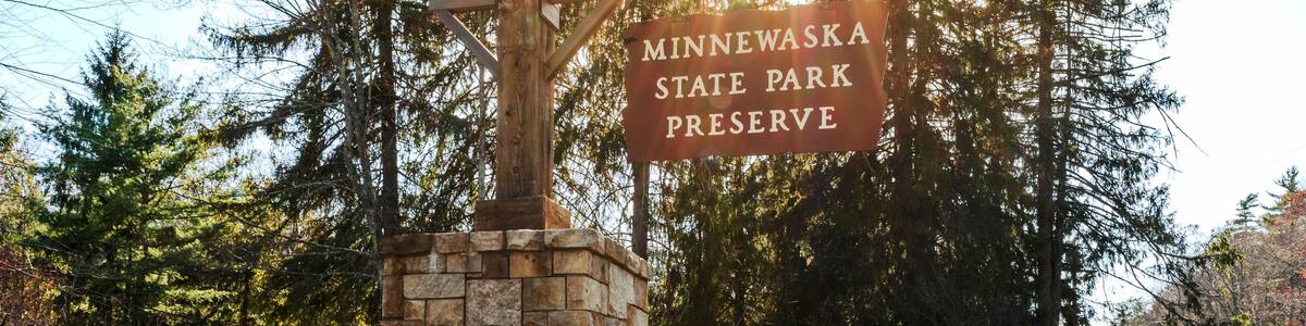 Kerhonkson, NY - US - Apr 23, 2025 Sunlight filters through tall pines at the entrance to Minnewaska State Park Preserve, where a rustic stone sign welcomes visitors to explore nature's beauty.