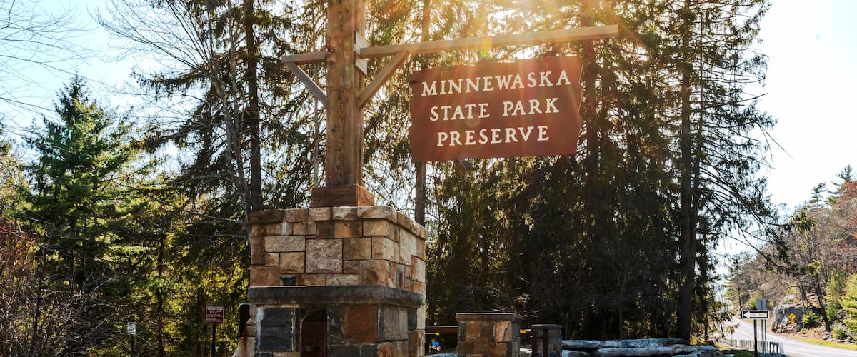 Kerhonkson, NY - US - Apr 23, 2025 Sunlight filters through tall pines at the entrance to Minnewaska State Park Preserve, where a rustic stone sign welcomes visitors to explore nature's beauty.
