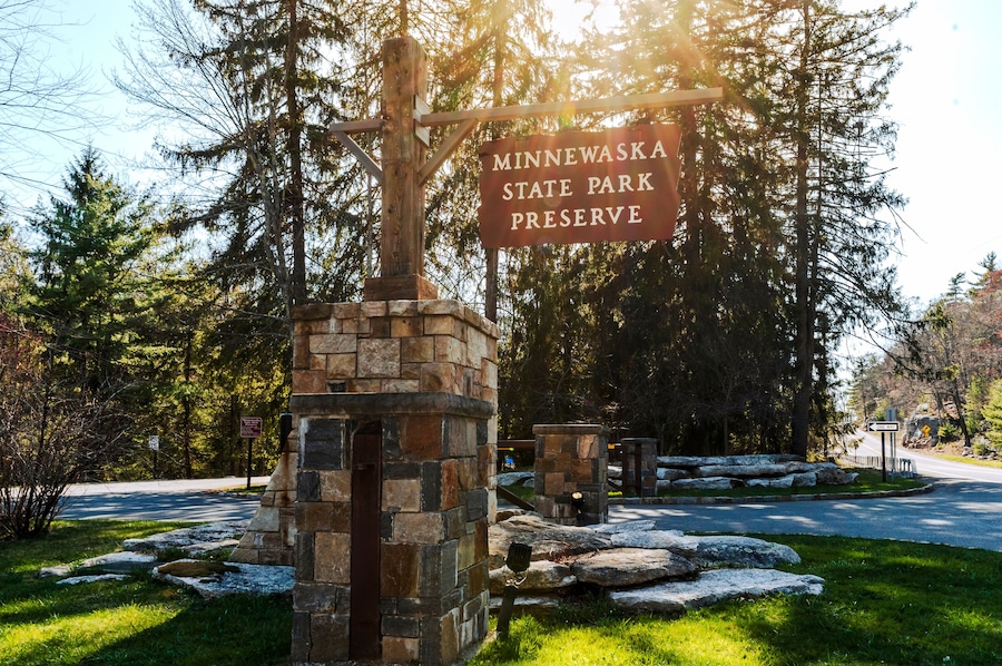Kerhonkson, NY - US - Apr 23, 2025 Sunlight filters through tall pines at the entrance to Minnewaska State Park Preserve, where a rustic stone sign welcomes visitors to explore nature's beauty.