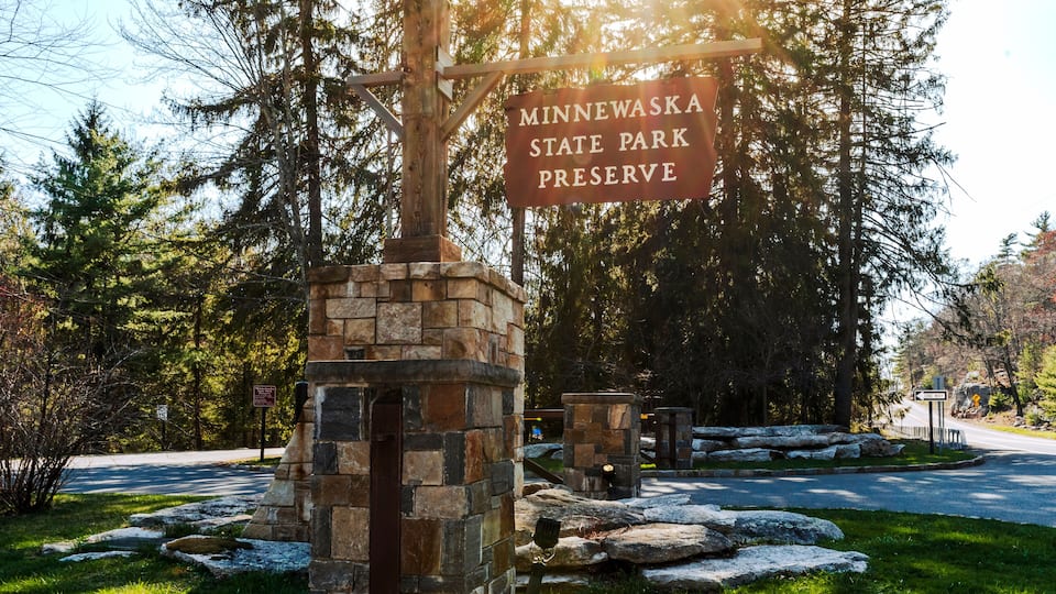 Kerhonkson, NY - US - Apr 23, 2025 Sunlight filters through tall pines at the entrance to Minnewaska State Park Preserve, where a rustic stone sign welcomes visitors to explore nature's beauty.