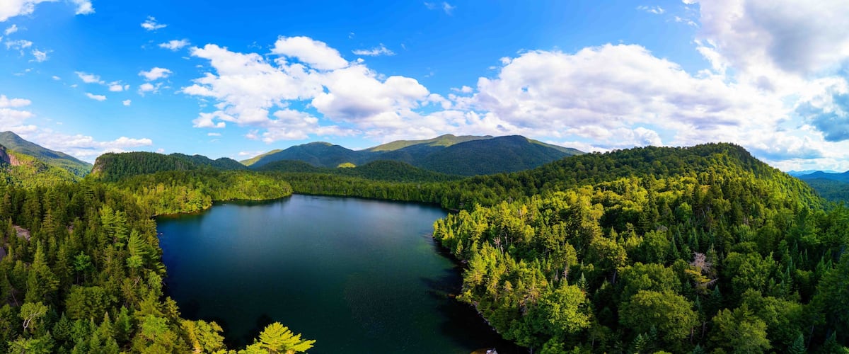 A serene lake surrounded by dense forest and mountains under a clear sky.