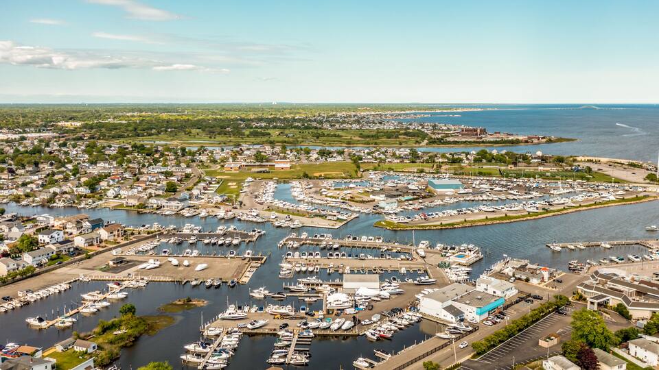 A marina with numerous boats docked, surrounded by residential buildings and a large body of water.