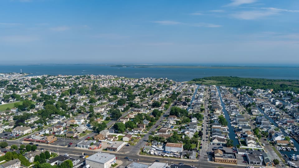 An aerial view of a coastal town with dense housing, a marina, and a clear view of the ocean.