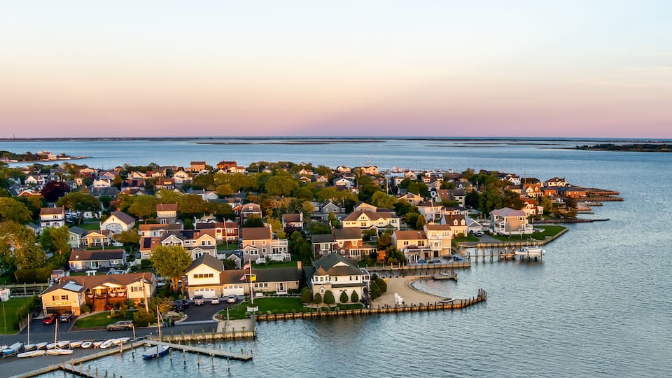 A coastal residential area with houses, a marina, and a pier extending into the water.