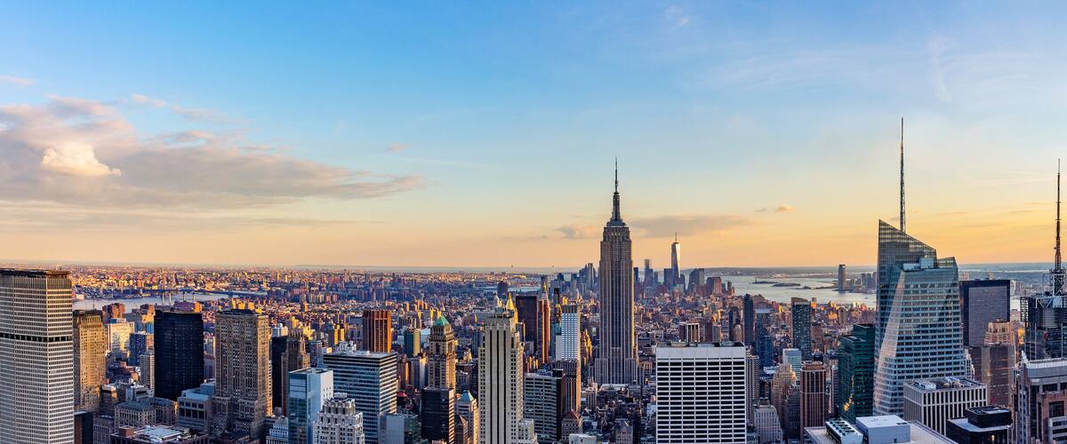 A cityscape with numerous skyscrapers, including the Empire State Building, under a clear sky.