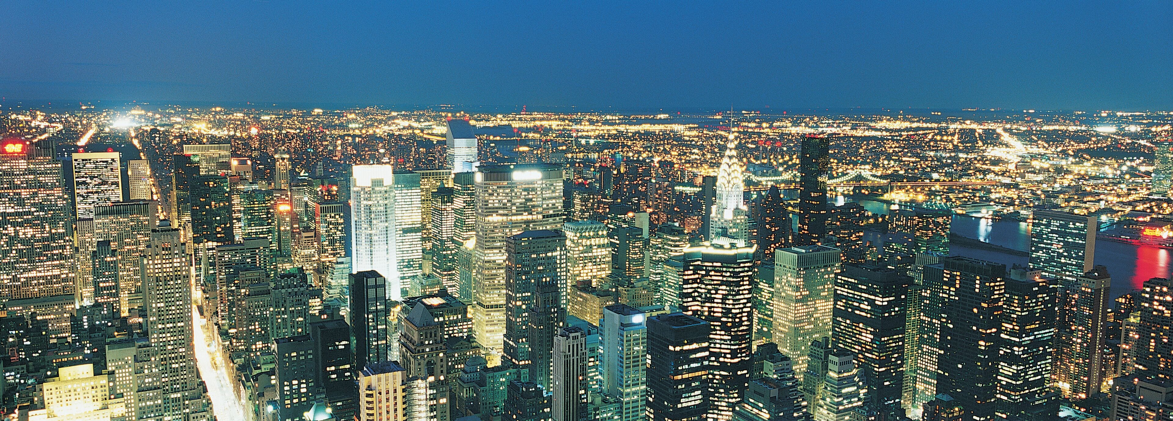 A densely packed cityscape with numerous high-rise buildings and a river in the background.