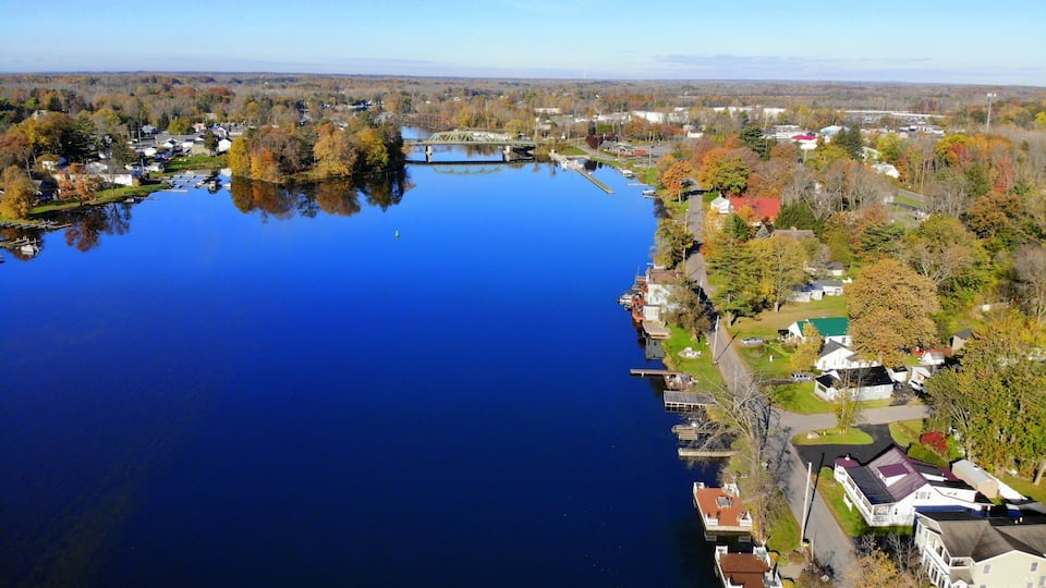 A river with a bridge, surrounded by autumn-colored trees and residential buildings.