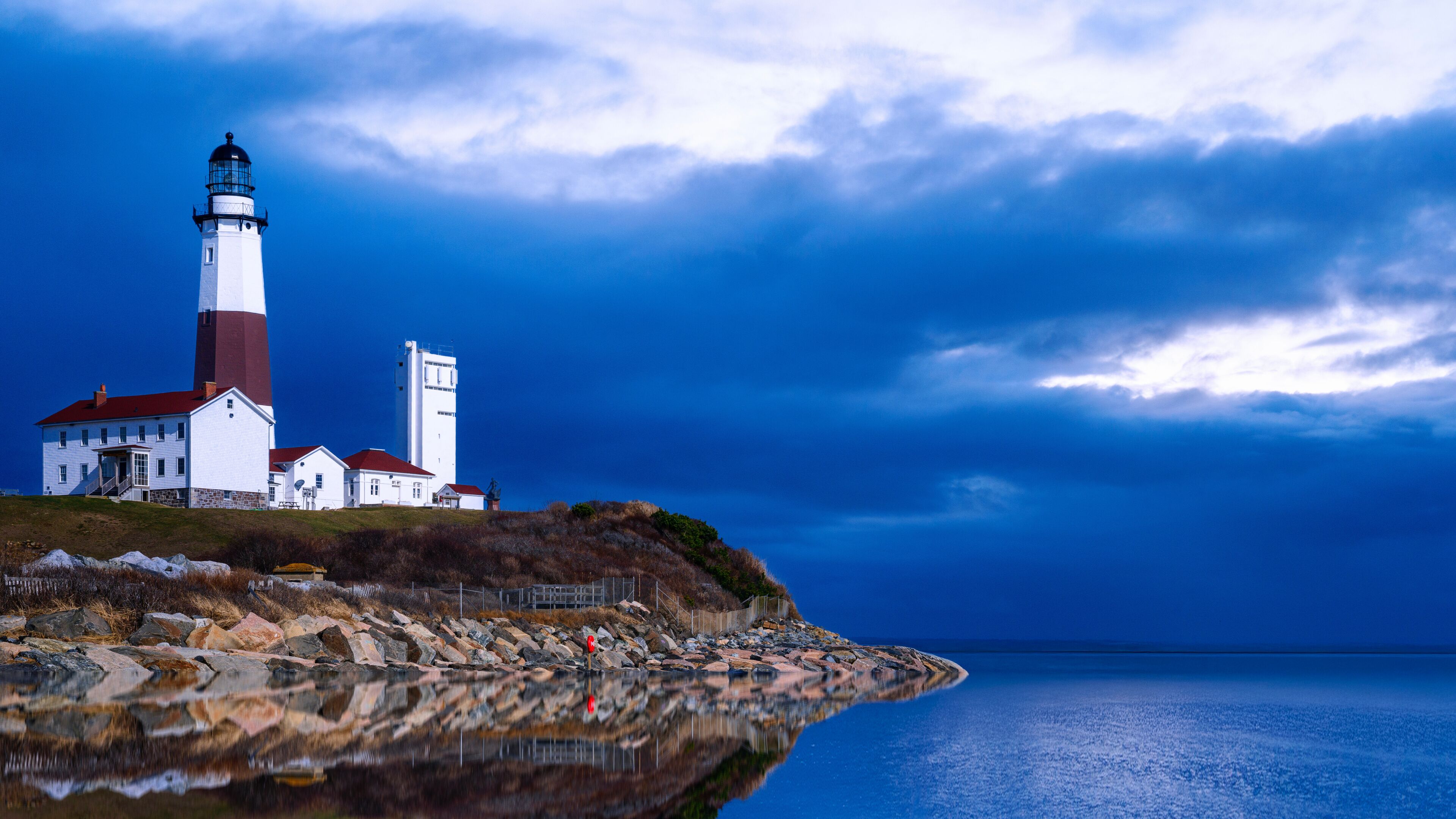 Montauk Point Light on top of the rocky hill with dramatic seascape, clouds, horizon, and ocean reflections in Long Island, Suffolk County, New York, USA.