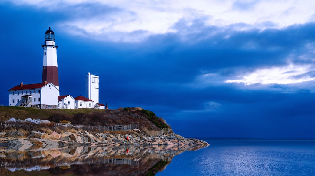 Montauk Point Light on top of the rocky hill with dramatic seascape, clouds, horizon, and ocean reflections in Long Island, Suffolk County, New York, USA.
