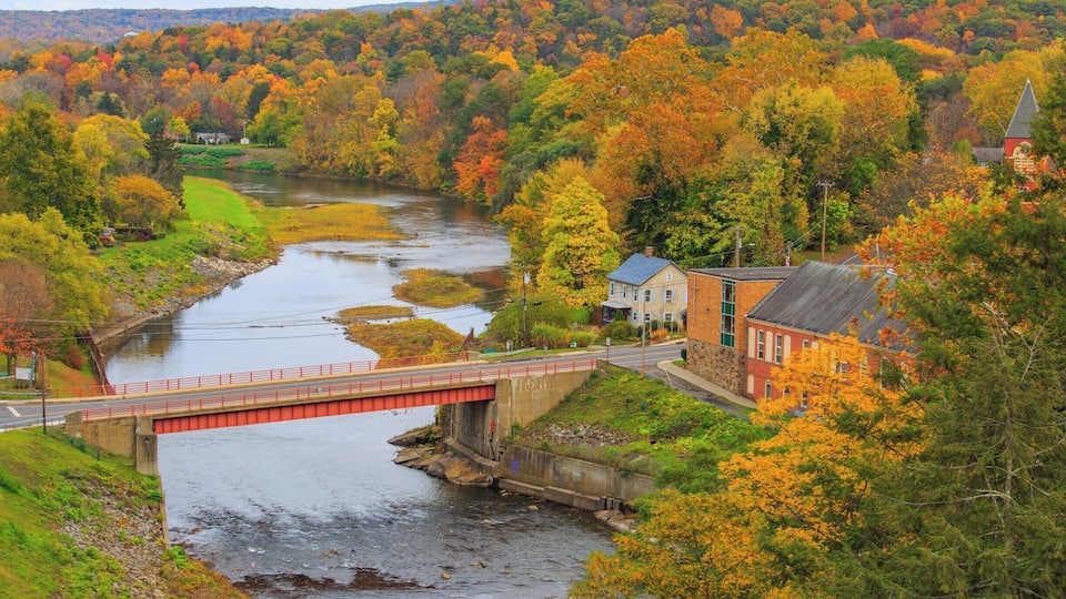 A river flowing through a valley with autumn-colored trees, a red bridge, and a church with a steeple.