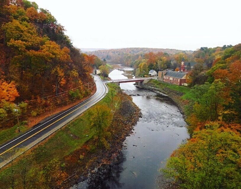 A river flowing through a valley with autumn foliage, a bridge, and a road curving alongside.