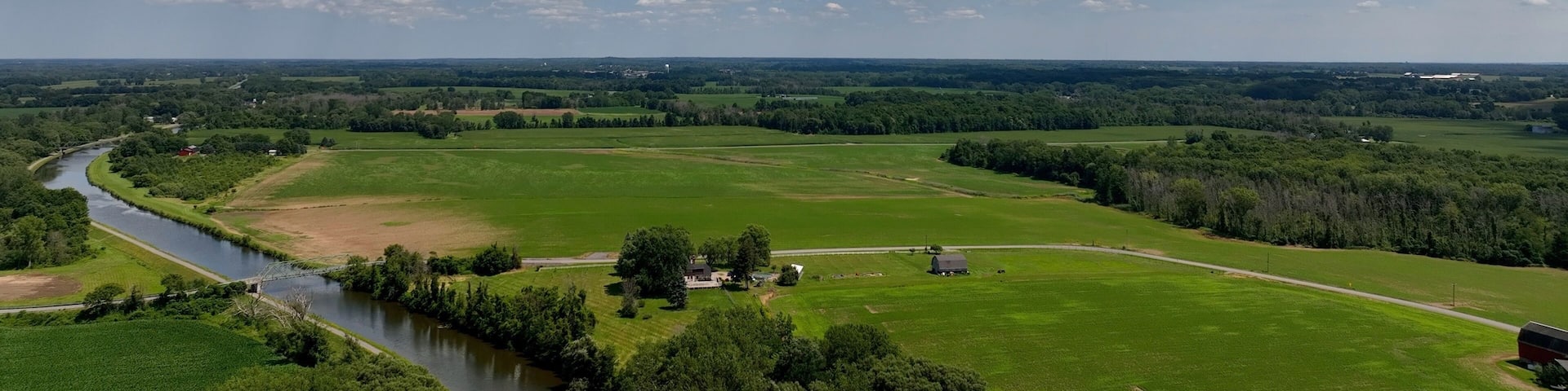Landscape with green farmland by Eire Canal in Up State New York under blue sky and clouds on summer day
