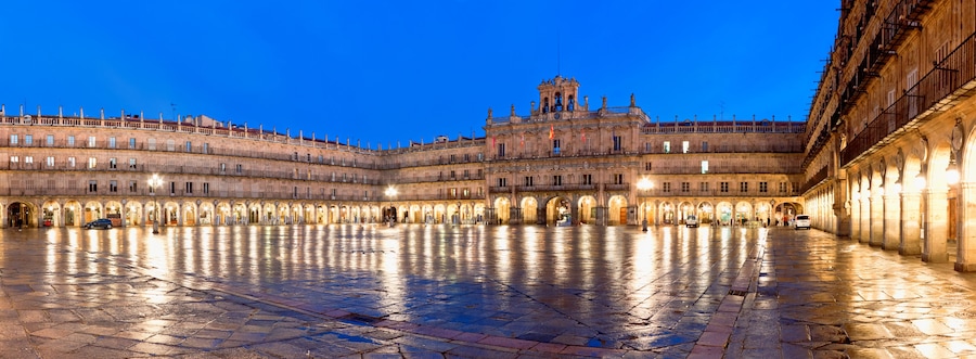 Una plaza histórica con un amplio espacio abierto, edificios ornamentales y una imponente torre de campanas.