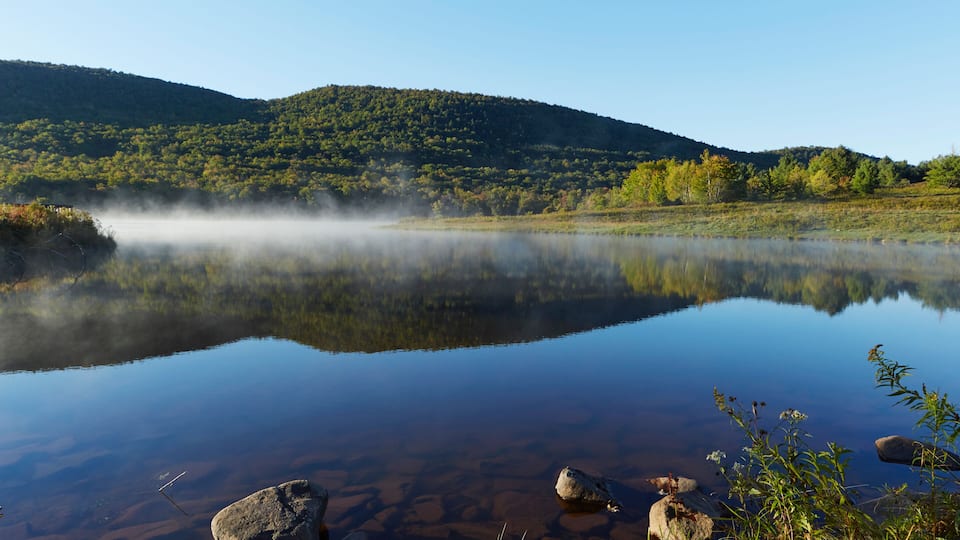 A calm lake with clear reflections, surrounded by green hills and rocks.