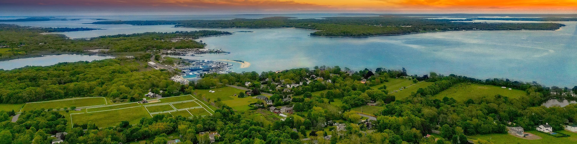 A coastal landscape with a sunset, a marina, and a residential area.