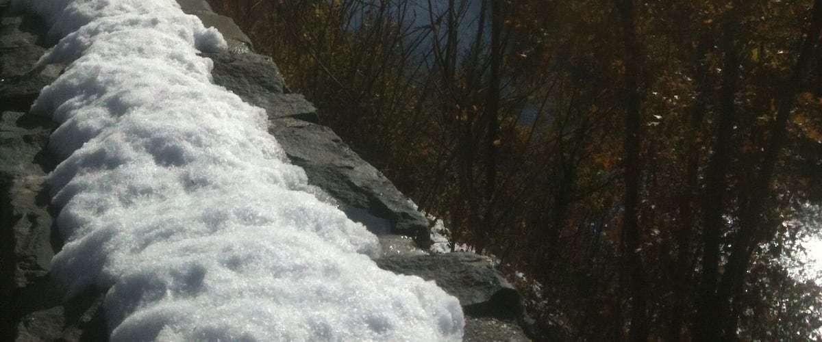 A snow-covered stone wall, a river, and autumn trees.