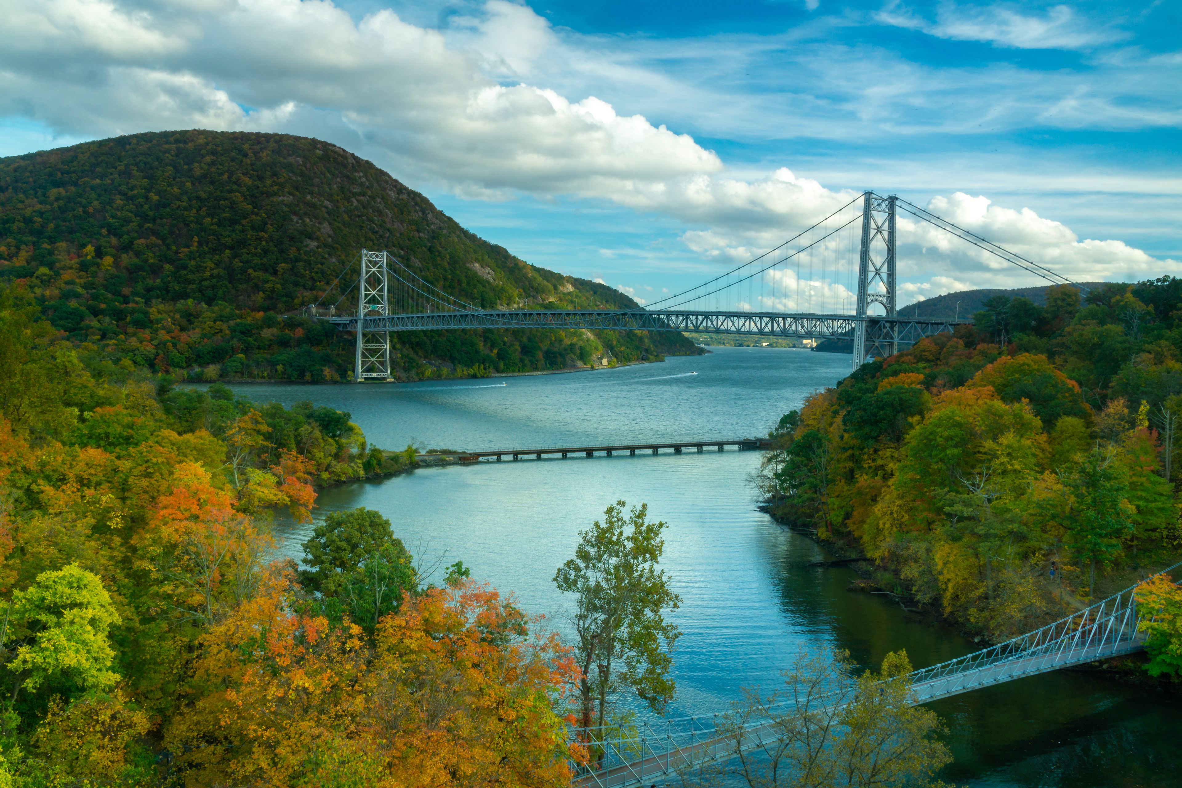 Un pont suspendu enjambant une rivière, entouré d’arbres et de collines aux couleurs automnales.