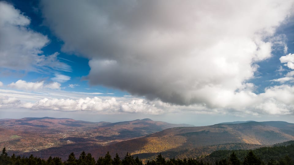 A mountainous landscape with autumn foliage, a clear sky, and scattered clouds.