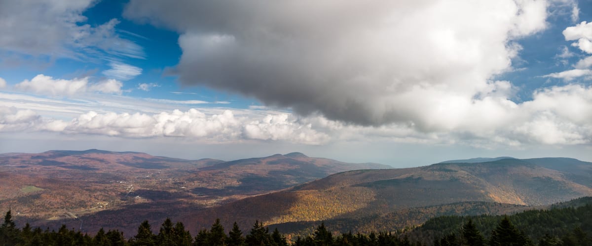 A mountainous landscape with autumn foliage, a clear sky, and scattered clouds.