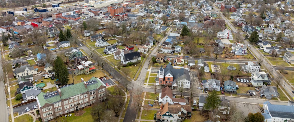 An aerial view of a town with a mix of residential houses, a large industrial complex, and a prominent red brick building.