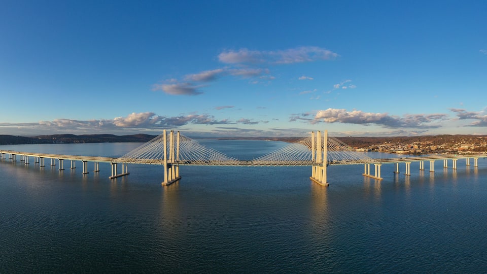 A large suspension bridge spanning a wide river, with a cityscape in the background.