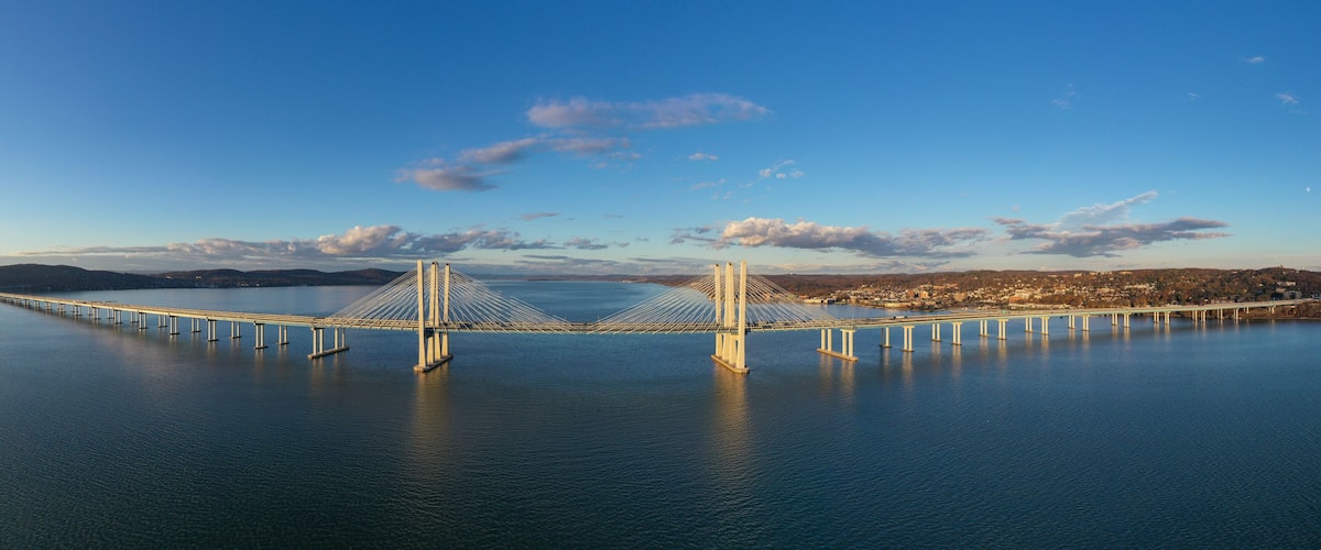 A large suspension bridge spanning a wide river, with a cityscape in the background.