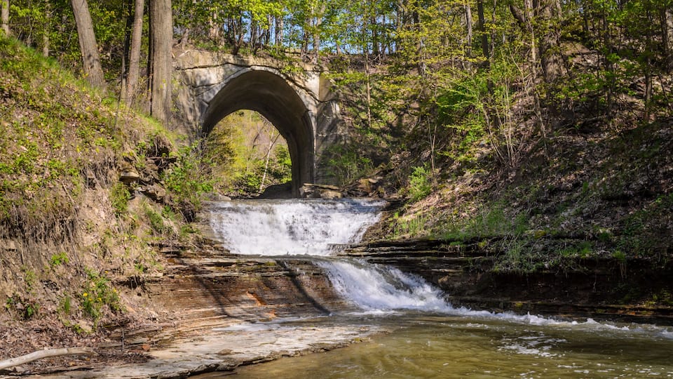 A stone bridge over a waterfall in a forested area.