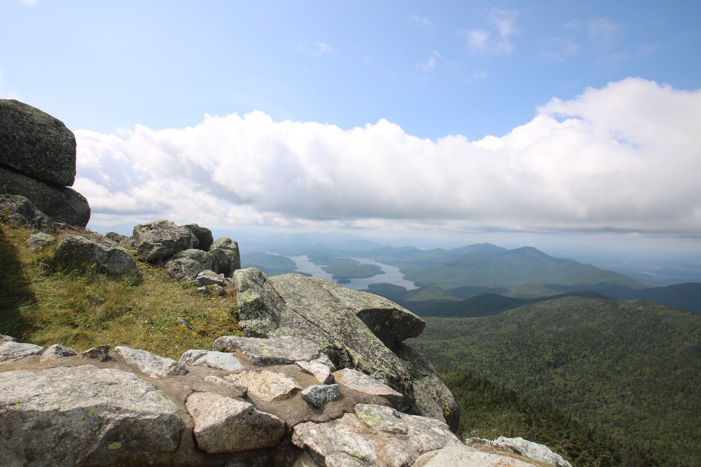 A mountainous landscape with rocky terrain and a distant view of a lake surrounded by hills.